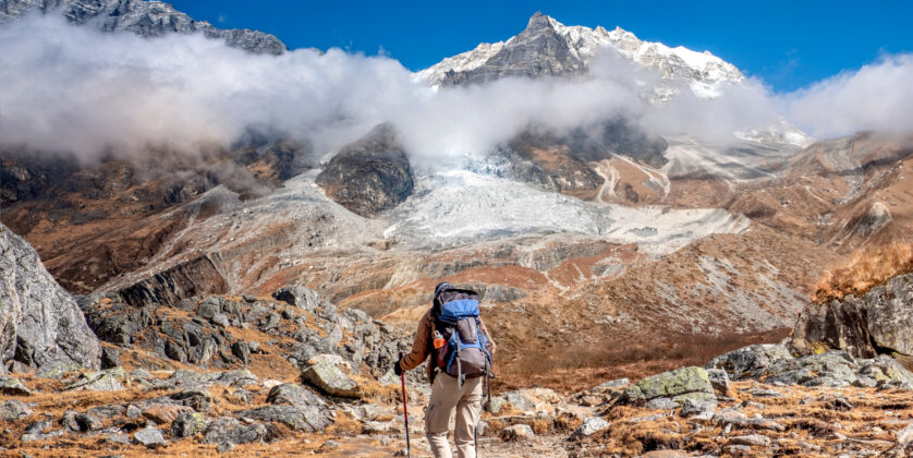 A scenic view of Langtang Valley, surrounded by towering snow-capped peaks and lush green valleys, with trekkers on the trail.