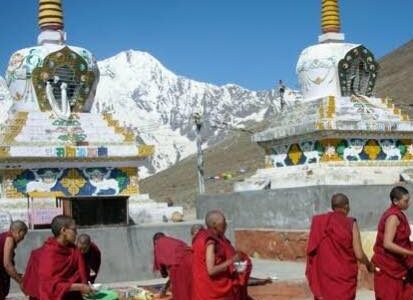 Buddhist monks in maroon robes engaged in philosophical debate in a monastery courtyard, with traditional white stupas and snow-covered Himalayan peaks in the background