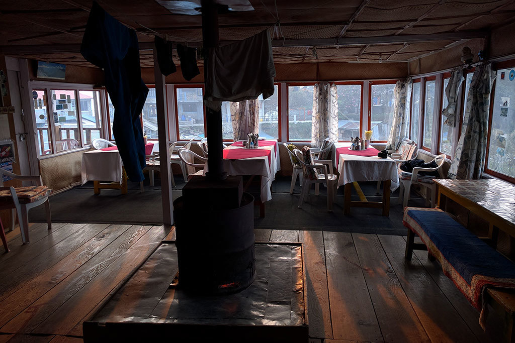 Traditional Himalayan tea house interior with wooden floors, tables, chairs, and a central stove for warmth in a mountain region.