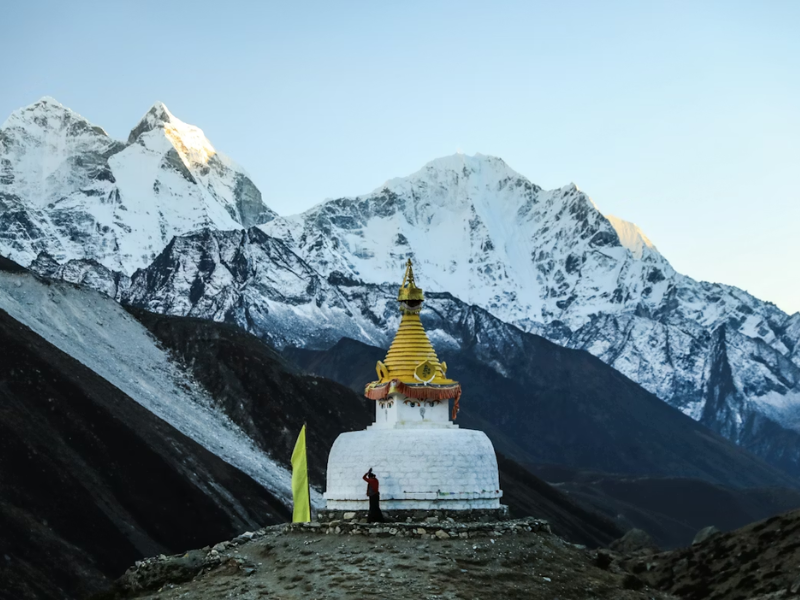 Sherpa performing a Buddhist prayer ritual at a Himalayan stupa during pre-sunset along the Everest Base Camp trek, with snow-covered peaks in the background.