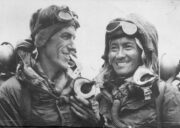 Black and white photograph of two mountaineers wearing oxygen equipment and cold-weather gear, smiling after reaching the summit of Mount Everest on 29 May 1953.