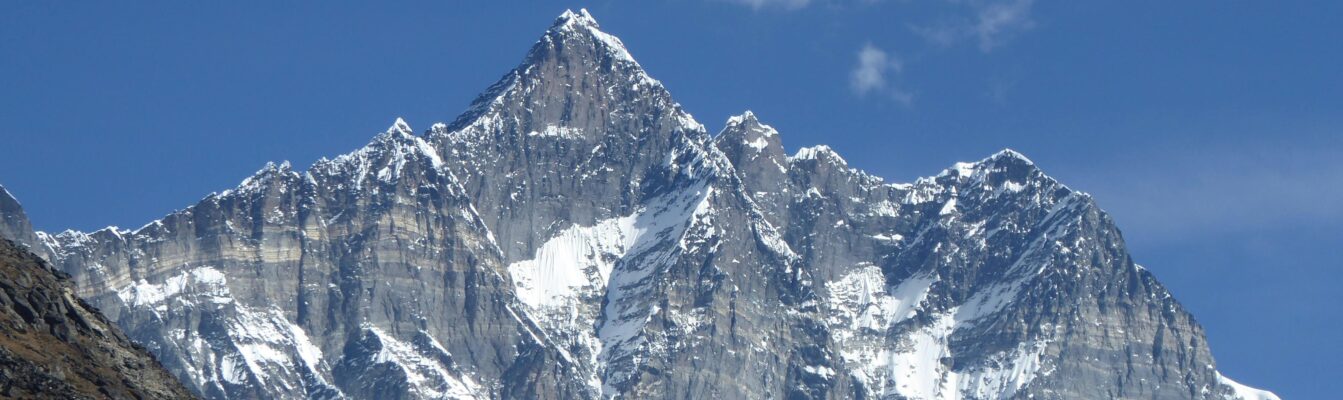 Snow-covered Himalayan peak with steep rock faces rising above Dingboche under a clear blue sky in March.