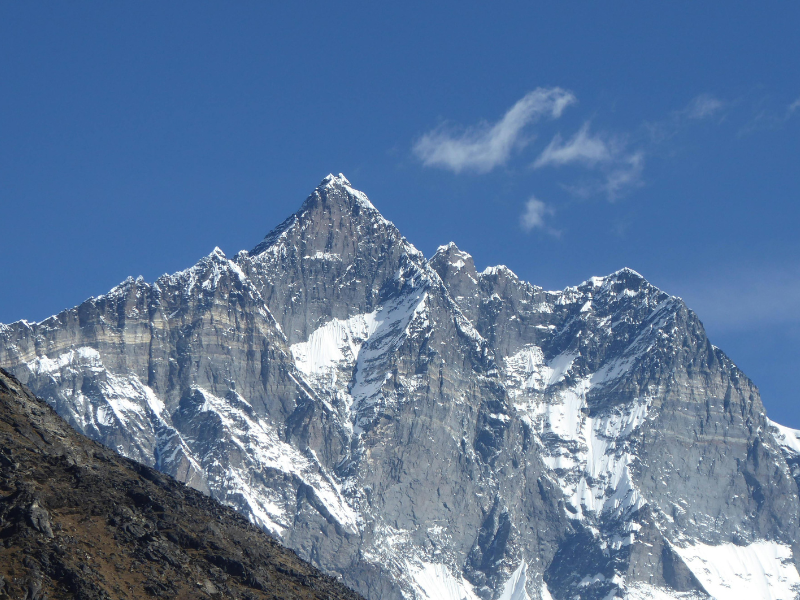 Snow-covered Himalayan peak with steep rock faces rising above Dingboche under a clear blue sky in March.