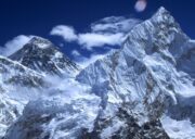 Snow-covered south face of Mount Nuptse with Mount Everest rising behind it under a deep blue winter sky in the Himalayas.