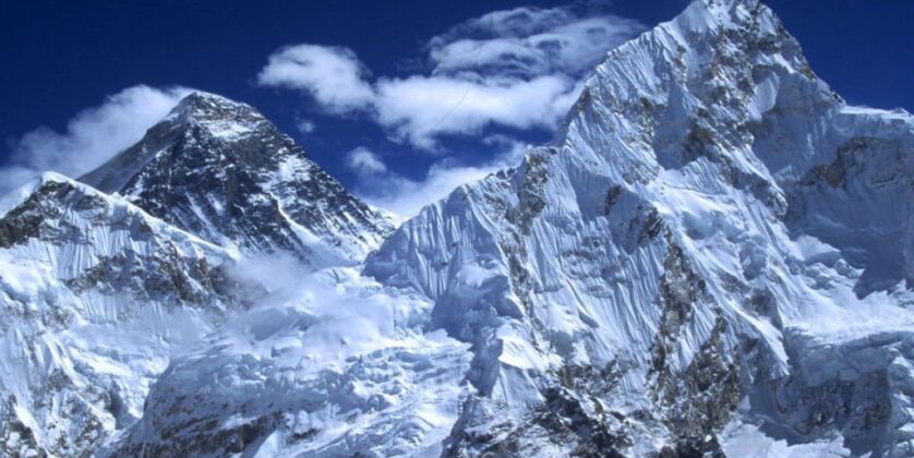 Snow-covered south face of Mount Nuptse with Mount Everest rising behind it under a deep blue winter sky in the Himalayas.