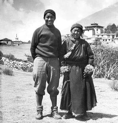 Historic black-and-white photograph of a Himalayan mountaineer walking with his mother on a mountain path before a major Everest expedition, near a Buddhist monastery in Nepal, 1953.