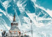 Snow-covered Mount Lhotse rising behind a Buddhist stupa along the Everest Base Camp trekking route, with prayer flags and trekkers in the foreground.