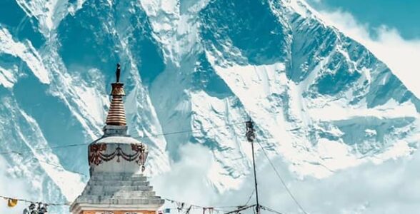 Snow-covered Mount Lhotse rising behind a Buddhist stupa along the Everest Base Camp trekking route, with prayer flags and trekkers in the foreground.