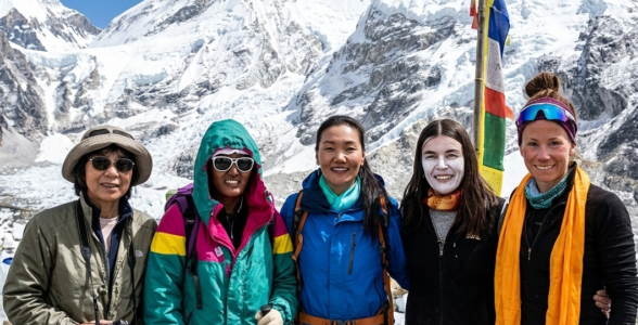 A group of five legendary female mountaineers standing together at the Everest Base Camp, with Mount Everest in the background.
