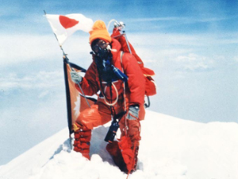 Junko Tabei, the first woman to summit Mount Everest in 1975, holding flags at the summit.