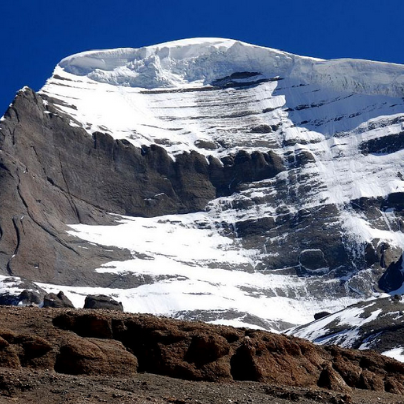 East face of Mount Kailash with layered snow and rock under a clear blue sky