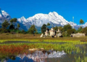 Lush green fields and small stone shrines in Kerung (Kyirong) with snow-capped Himalayan peaks reflected in a calm water pool.