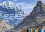 Mount Kailash with Nandi Parvat in front, framed by colorful prayer flags along the rocky pilgrimage trail.