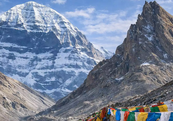 Mount Kailash with Nandi Parvat in front, framed by colorful prayer flags along the rocky pilgrimage trail.