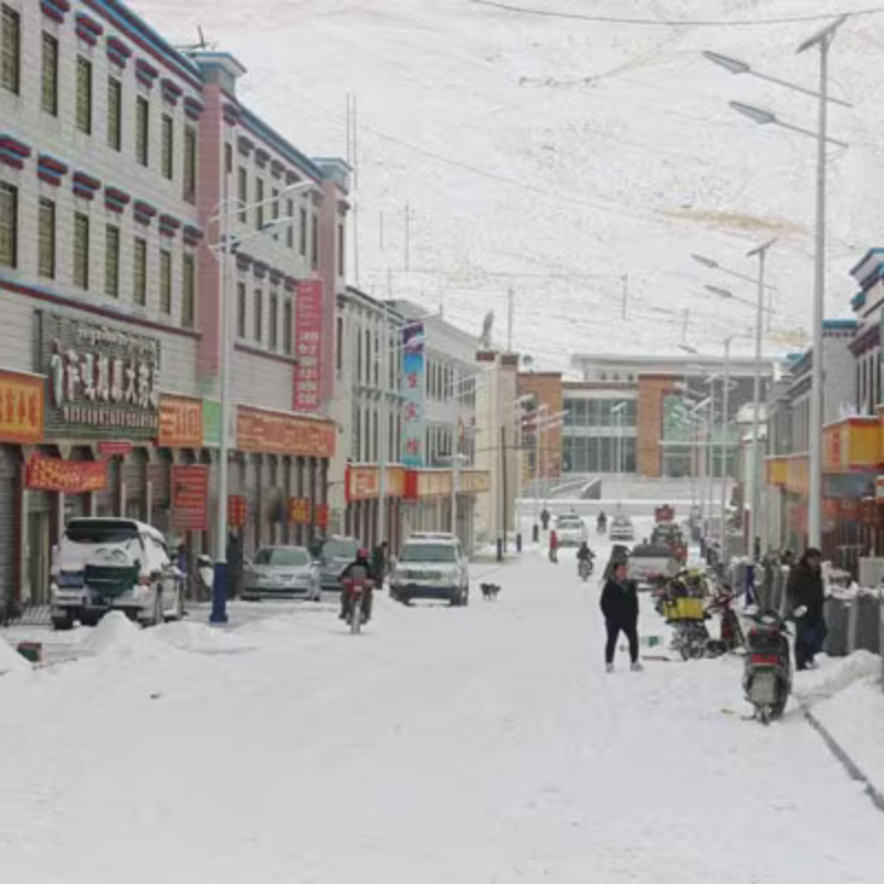 Snow-covered street in Saga, Tibet with shops, vehicles, and pedestrians in winter