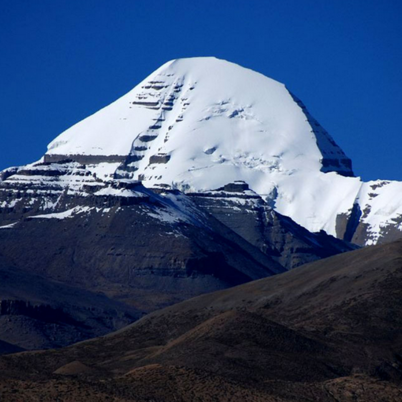 South face of Mount Kailash with snow-covered peak above dark rocky hills