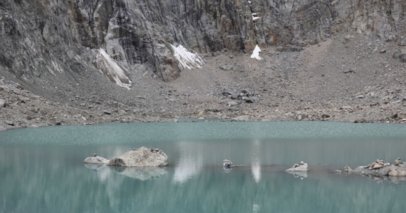 Close view of turquoise Gauri Kund lake surrounded by rocky cliffs near Dolma La Pass.
