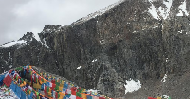 Prayer flags at Dolma La Pass surrounded by snowy rocky mountains