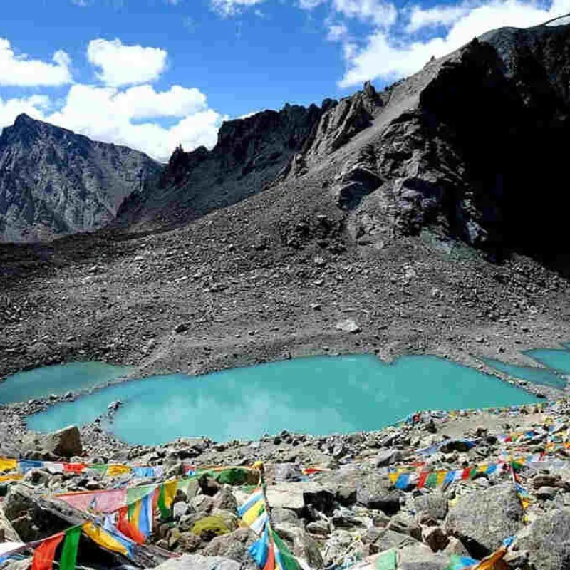 Turquoise Gauri Kunda lake with prayer flags near Dolma La Pass during spring in Tibet.