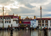 Jokhang Temple in Lhasa, Tibet, with pilgrims and visitors gathered in the courtyard on a rainy day beneath dramatic clouds and rising incense smoke.