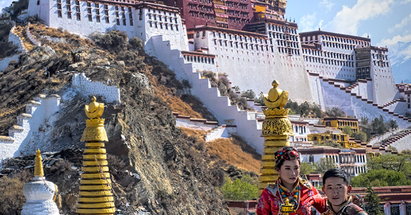 Potala Palace towering above Lhasa, Tibet, with visitors in traditional Tibetan clothing standing in the foreground against the historic white and red palace walls.