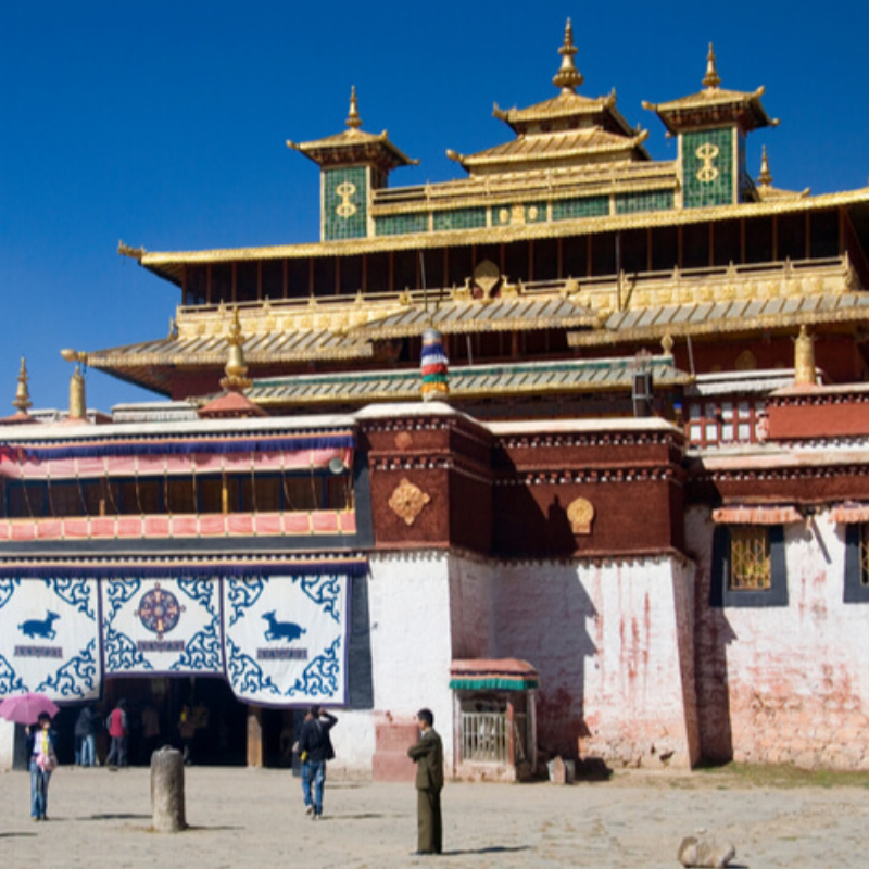 Front view of Sera Monastery's main assembly hall with golden roofs, traditional Tibetan architecture, and visitors at the entrance in Lhasa, Tibet.