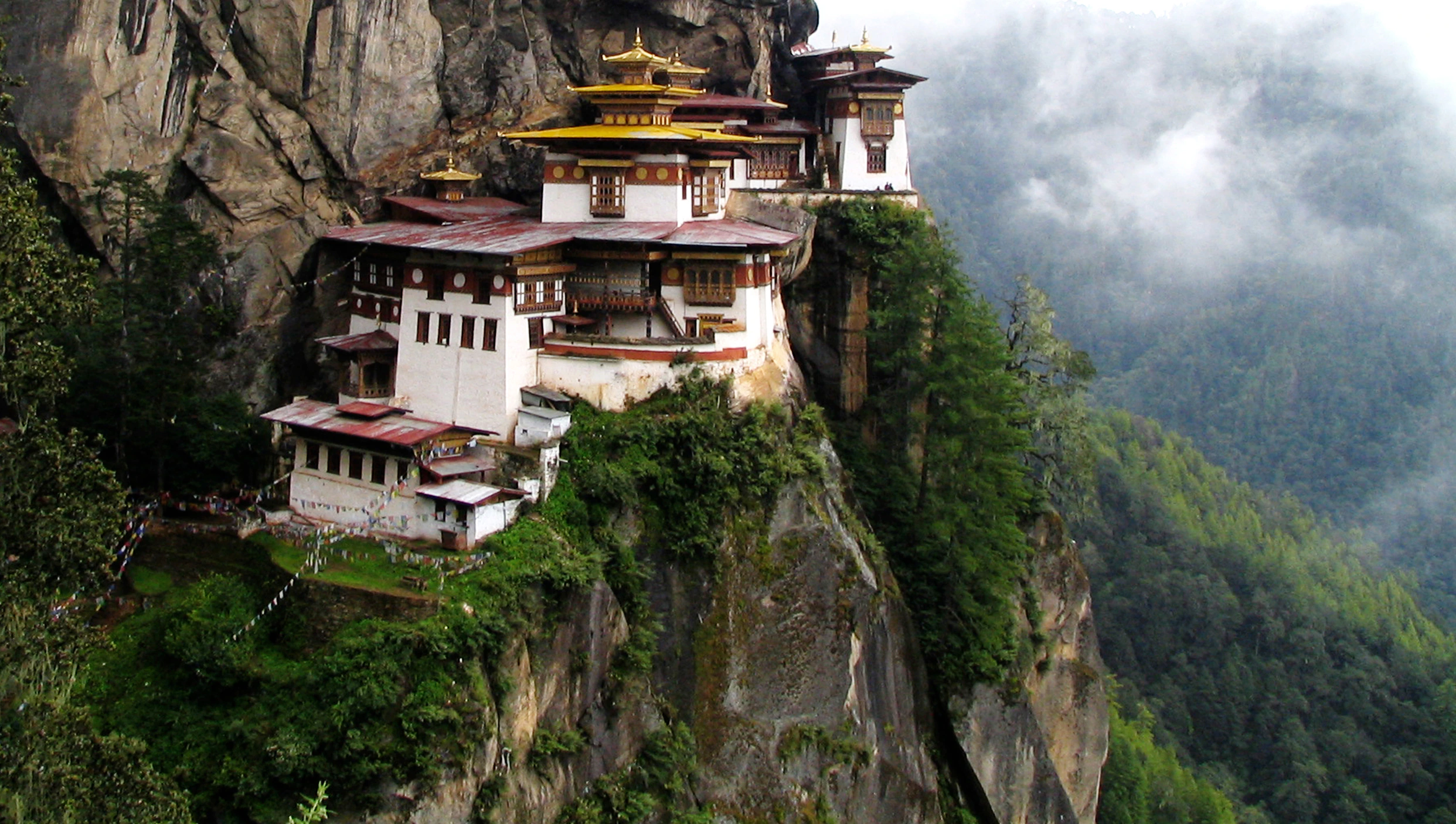 Monastery perched on a cliff face in a green Himalayan valley